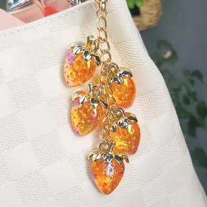 Close-up of iridescent resin strawberry keychain with gold-tone chain on a white bag.