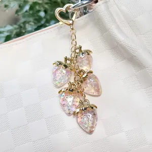 Detail view of shimmering resin strawberry charms on a gold heart-shaped keychain