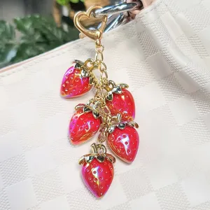 Close-up of vibrant red resin strawberry charms on a gold-tone heart keychain clasp.