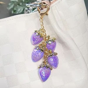 Close-up detail of a purple resin strawberry keychain with heart clasp on a white bag.