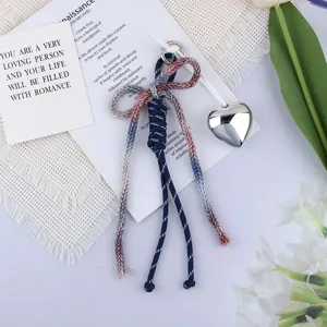 Detail view of a woven cotton rope bow bag charm with a silver heart pendant.