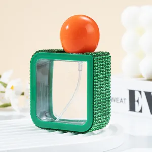 Detail showing a stylish 40ml square green rhinestone spray bottle with orange cap.