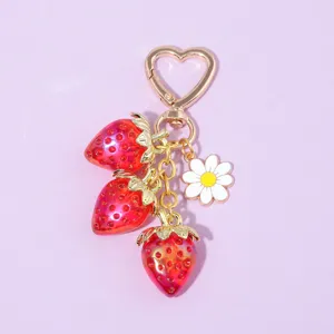 Close-up of translucent red strawberry and daisy charms on a gold heart keychain