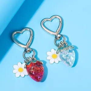 Close-up detail of translucent red and iridescent strawberry keychains with daisy charms