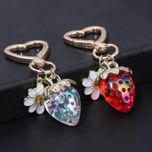 Close-up of sweet iridescent strawberry and daisy charms on a heart-shaped keychain clasp.