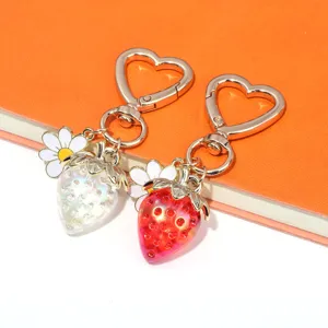 Detail of translucent red and white strawberry keychains with heart clasps and daisy charms