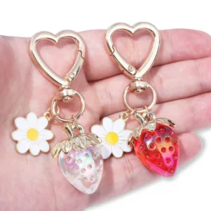 Macro detail of translucent strawberry and daisy charms on a heart-shaped keychain.
