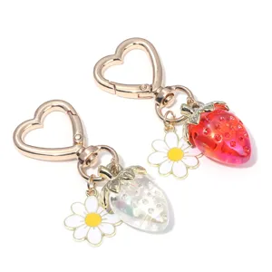 Close-up of translucent strawberry and daisy flower keychains with gold heart clasp