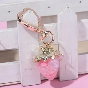 Close-up of a pink strawberry keychain with heart-shaped clip and gold leaf details