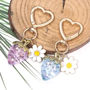 Detail view of translucent strawberry and daisy flower charms on a gold heart-shaped keychain
