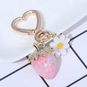 Close-up of translucent pink strawberry and daisy charms on a gold heart keychain.