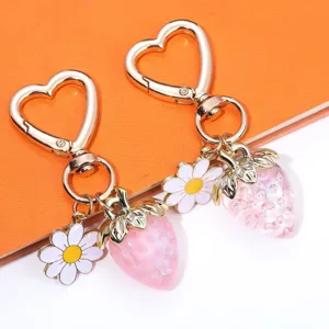 Close-up of translucent pink strawberry and daisy charms on heart-shaped gold keychains.