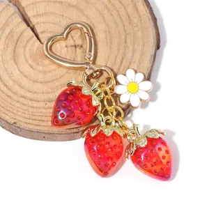 Close-up of translucent red strawberry charms with heart-shaped gold keychain clasp