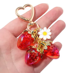 Close-up of translucent red strawberry and white daisy charms on a gold heart keychain