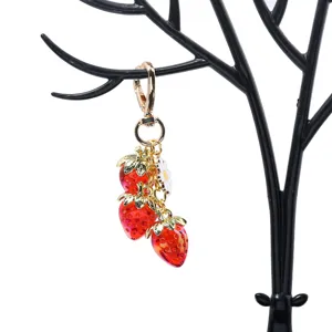 Close-up detail of a translucent red strawberry keychain hanging on a black jewelry stand
