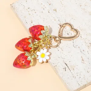 Close-up of translucent red strawberry keychain with white daisy and gold heart clasp