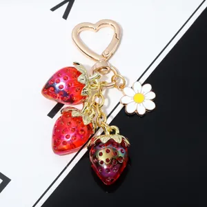 Close-up of translucent red strawberry charms and white daisy on heart-shaped keychain