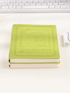 Detailaufnahme eines grünen B6 Notizbuchs aus Leder mit geprägtem Cover auf einem hellen Schreibtisch.