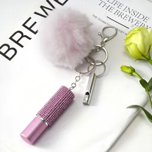 Gros plan d'un porte-clés avec pompon rose, bouteille en strass et sifflet d'argent.