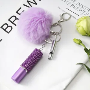 Gros plan d'un porte-clés flacon de parfum en strass violet avec pompon et sifflet