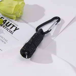 Detailed macro view of black rhinestone-studded mini LED flashlight with metal carabiner