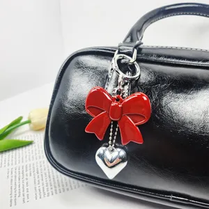 Close-up of red acrylic bow keychain with silver heart pendant on a black bag