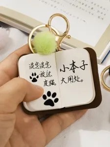 Mini PU leather notebook keychain close-up, cute pendant detail with furry pom-pom charm.