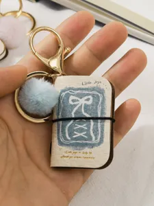 Miniature book keychain with blue pom pom charm, cute PU leather pocket notebook pendant.