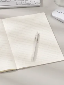 Vista detallada de un cuaderno de líneas minimalista abierto con un bolígrafo blanco.