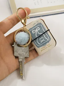 Mini PU leather book keychain pendant with cute plush ball and metal key charm for bags and keys.