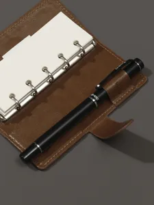 Carnet de poche à anneaux en cuir marron avec anneaux métalliques et stylo noir pour le quotidien.