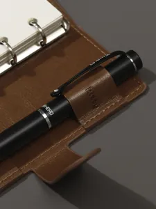 Vue détaillée d'un carnet à anneaux en cuir marron avec stylo noir et anneaux en métal.