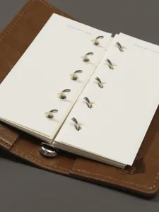 Vue de détail du carnet de notes en cuir marron avec anneaux métalliques et pages intérieures.