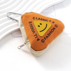 Detalle de un estuche triangular de lona naranja con diseño de cara sonriente y mosquetón