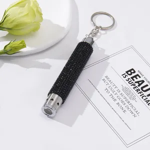 Close-up of a stylish black rhinestone LED flashlight keychain on a white surface.