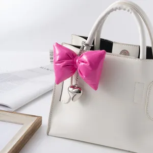 Close-up of hot pink puffy leather bow keychain with silver heart on a white bag