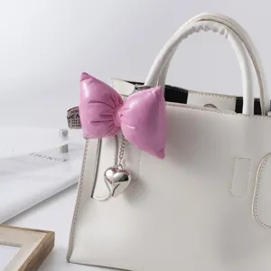Detail of a puffy pink bow keychain with a silver heart charm on a white handbag