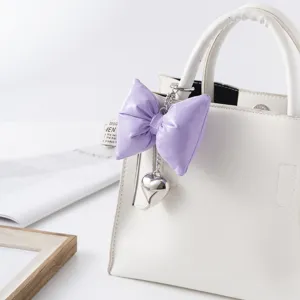 Close-up detail of purple puffed leather bow keychain with silver heart charm on white bag