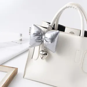 Detailed view of a stylish silver leather bow heart keychain hanging on a white handbag