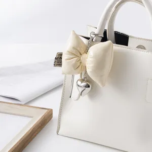 Detail of cream leather bow keychain with silver heart charm on a bag
