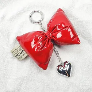 Close-up of shiny red leather puffed bow keychain with silver heart charm and tag.