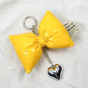 Detailed view of a yellow puffy leather bow keychain with a silver heart charm