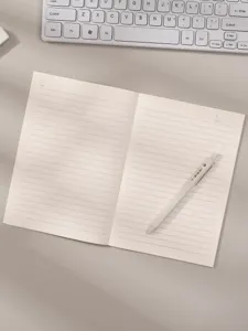 Primer plano de un cuaderno de líneas minimalista y un bolígrafo en un escritorio.