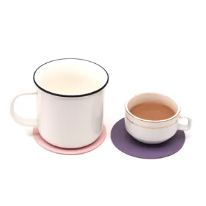 Detalle de posavasos de cuero redondos en rosa y púrpura con tazas de café blanco.