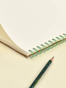 Nahaufnahme Detail eines A4 Spiral-Skizzenbuchs mit leeren Seiten und grünem Draht auf Tisch.