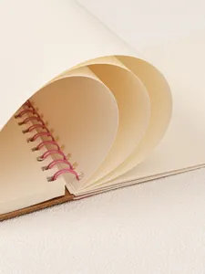 Close-up detail view of spiral sketchbook with cream pages and pink binding wire.