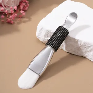 Close-up of a double-ended facial mask brush with soft bristles and a black rhinestone handle.