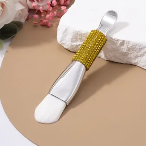 Close-up of dual-ended facial mask brush with gold rhinestone handle and silver spatula.
