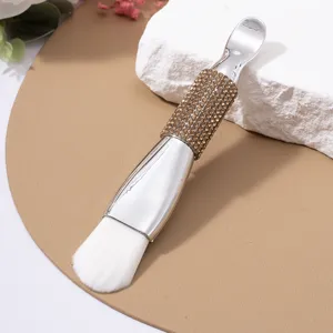 Close-up of double-ended facial mask brush with rhinestone handle and soft white bristles.