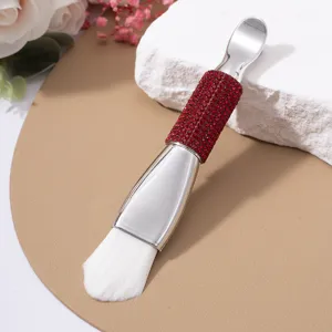 Close-up of double-ended facial mask brush with red rhinestone handle and soft white bristles